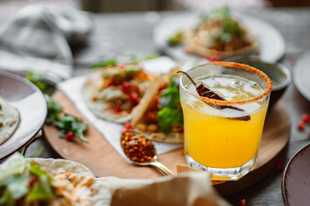Close-up of Mexican tacos and a spicy margarita cocktail on a wooden table.